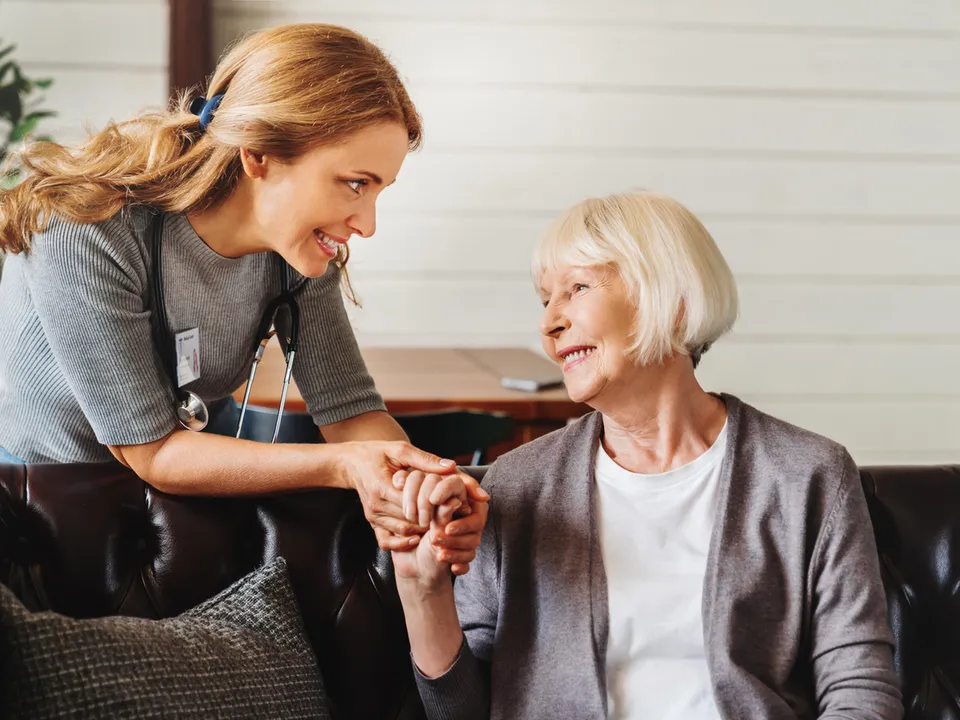 A home care aide holding an older woman's hands at home